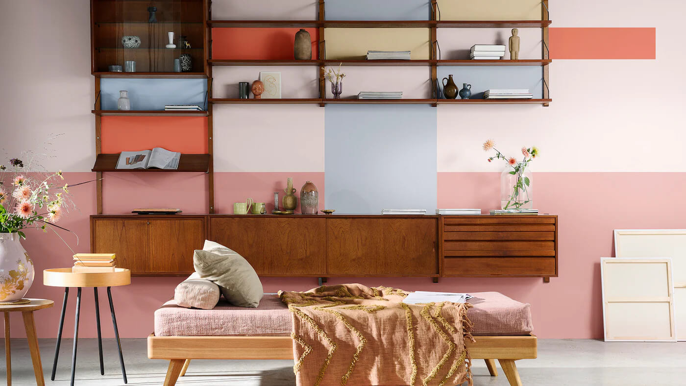 Sala de Estar decorada com uma pintura inspirada na colcha de retalhos atrás de uma estante aberta, com a paleta para Cores para Uma Casa Delicada e Afetiva das Tintas Coral. Tons mais quentes e inspiradores criando uma parede impactante e criativa.