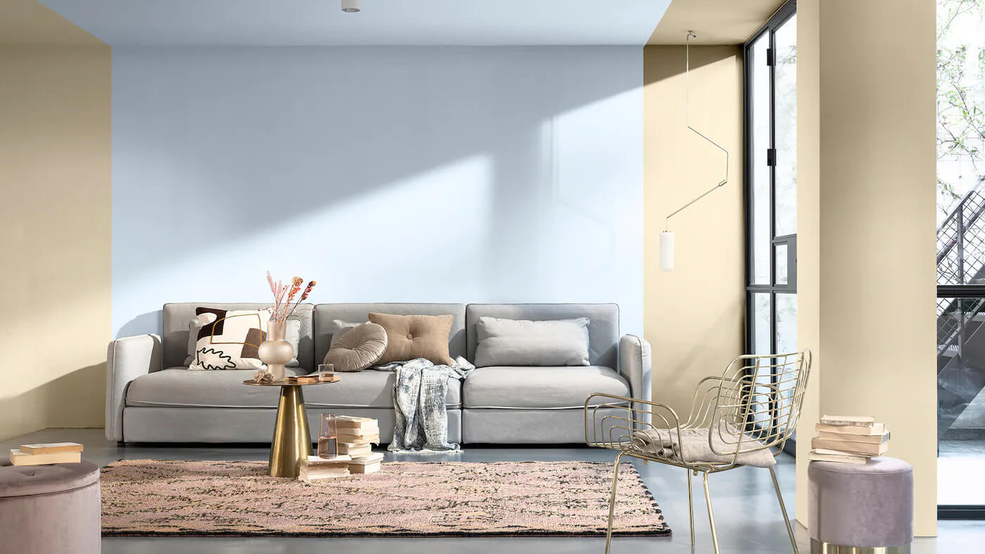 Sala de estar decorada com a cor Melodia Suave da Tintas Coral. A entrada de luz natural na sala evidência a composição do azul suave que demarca o sofá até o teto ao neutro natural nas laterais. O tom cinza do sofá com o Melodia Suave deixa o ambiente mais agradável.