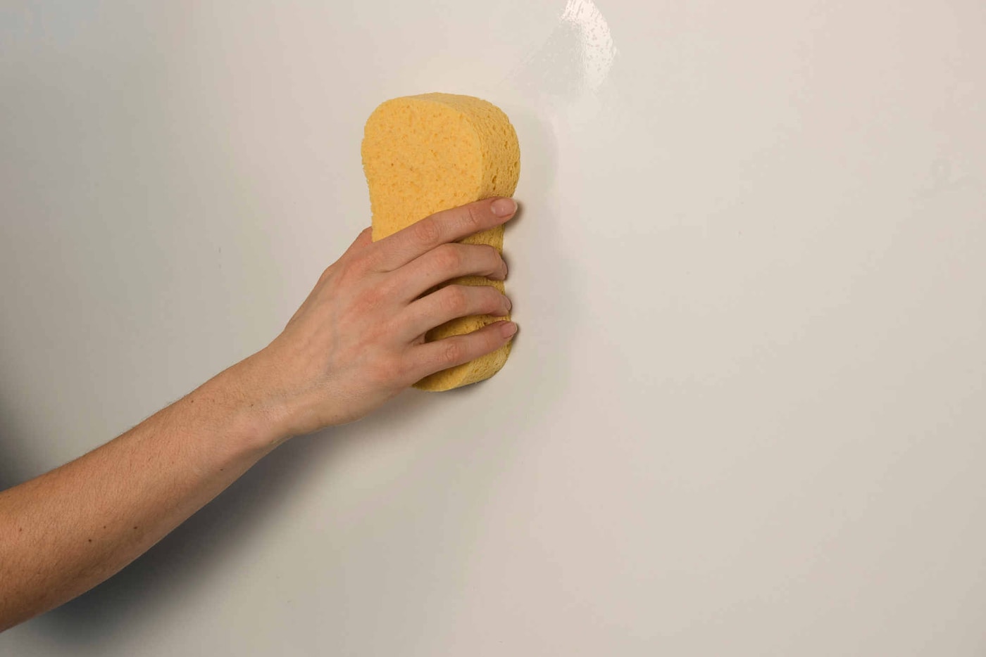Mężczyzna próbuje zmyć grzyb na ścianie za pomocą gąbki i wody