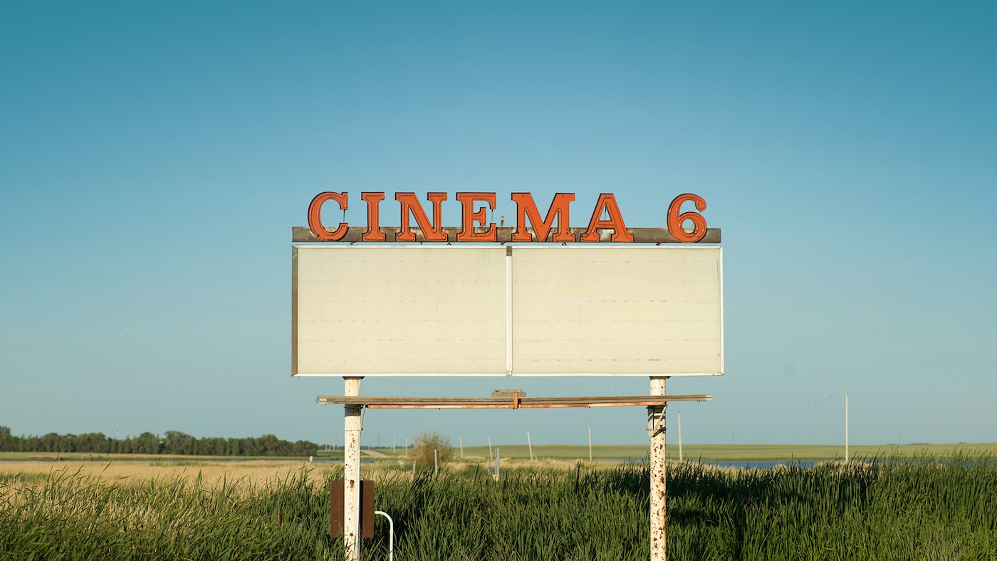 An orange cinema sign stands out against a blue sky.