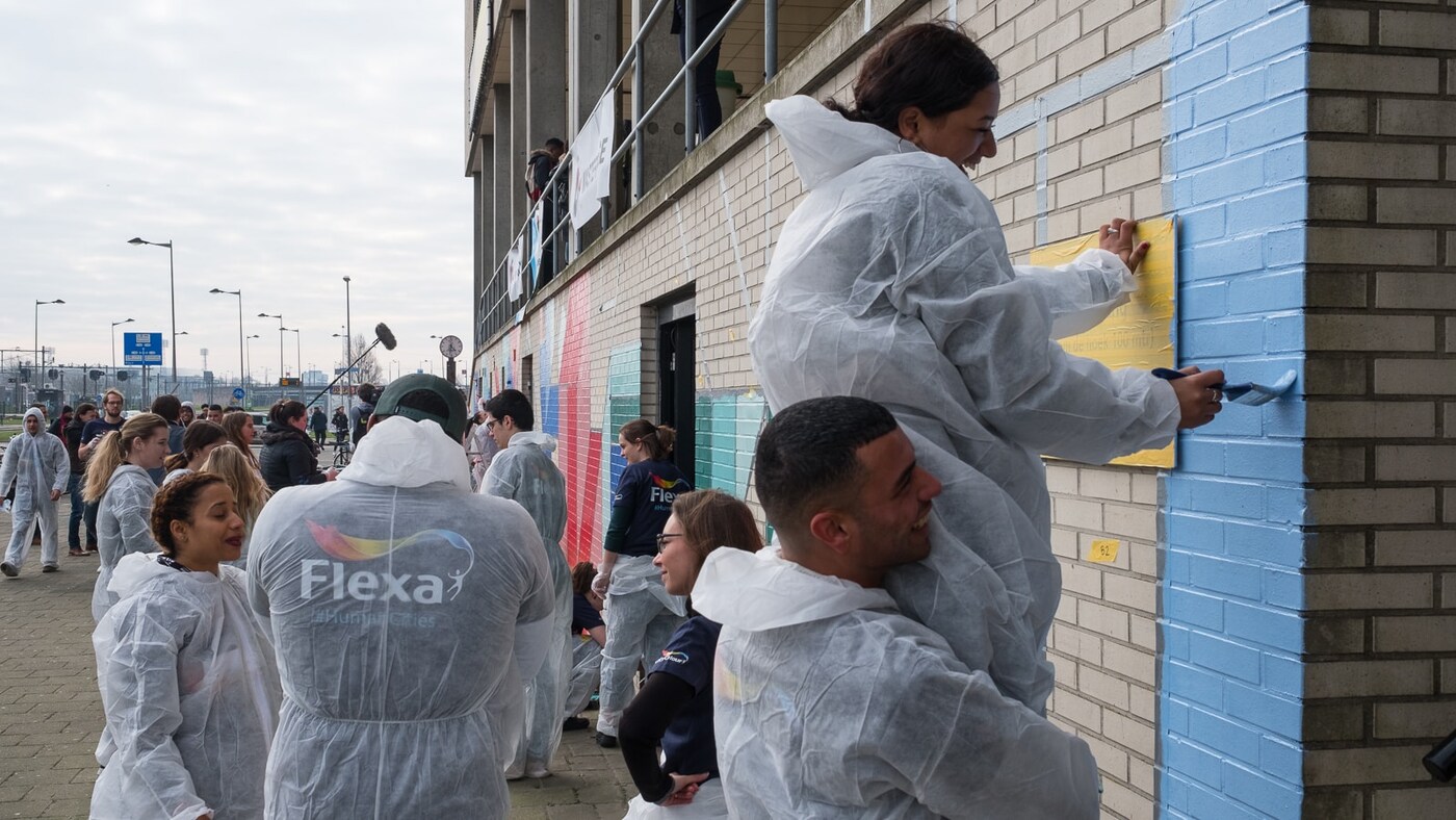 A man helps a woman to paint the wall.