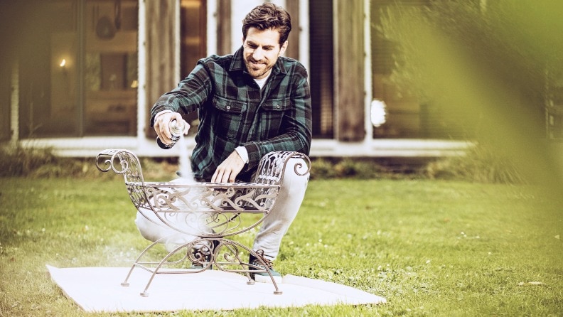 Mann mit einer Sprühdose Metallschutzlack von Hammerite in der Hand hinter einem weißen Metallobjekt in einem Garten.