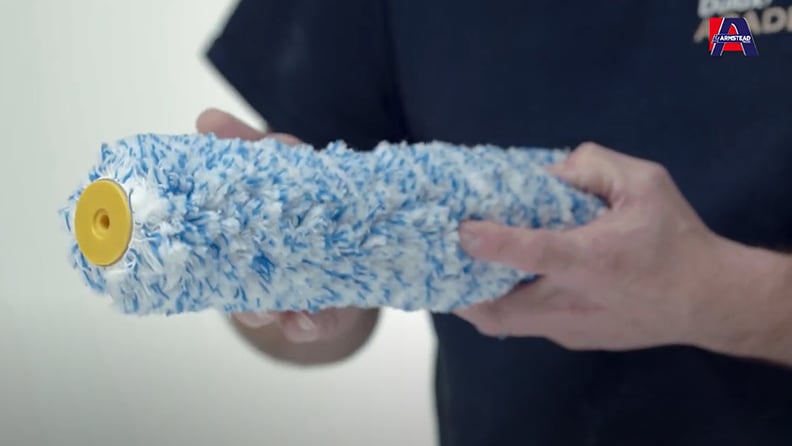 Hands holding a blue and white textured paint roller cover with yellow end cap, with the Armstead logo visible in the corner.