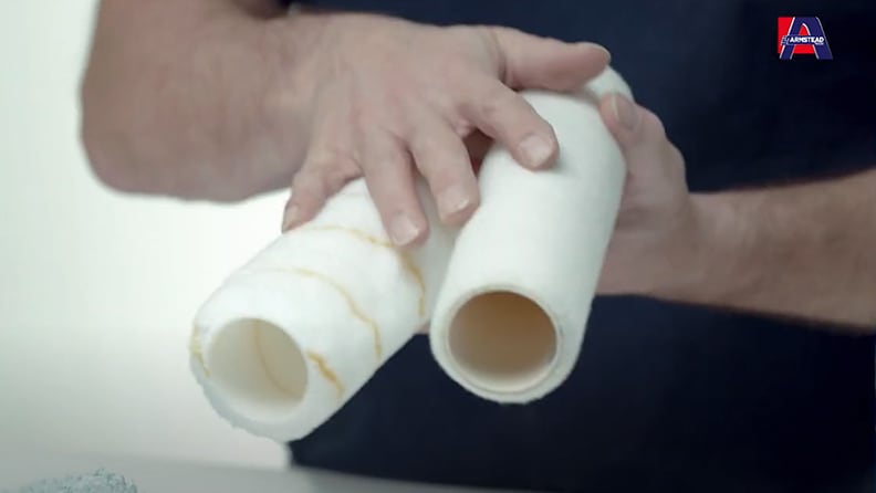 Close-up of hands holding two white paint roller covers, demonstrating their different textures and core sizes with the Armstead logo visible in the corner.
