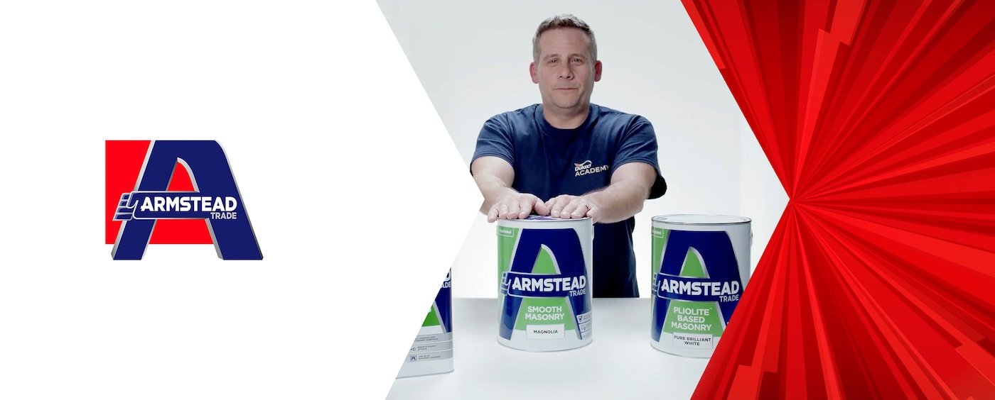 Professional painter in navy blue shirt standing behind two Armstead Trade masonry paint cans with the brand logo prominently displayed on a red and white geometric background.