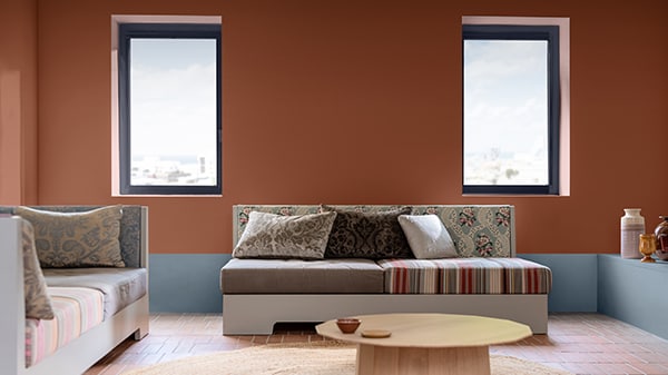 En stue med terracottafarvede vægge, lyseblå vægdetaljer, neutrale møbler, farverige mønstrede puder og et sofabord i lyst træ på et terracottafarvet klinkegulv.