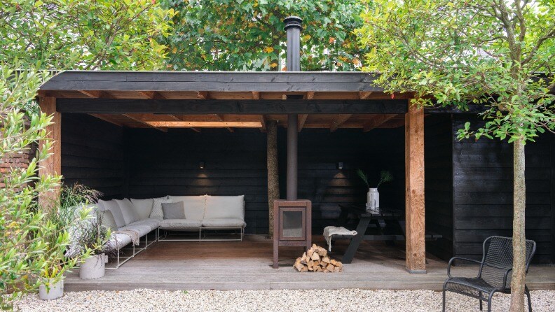 Überdachtes Outdoor-Wohnzimmer mit Lounge-Set, Kamin und Feuerholz