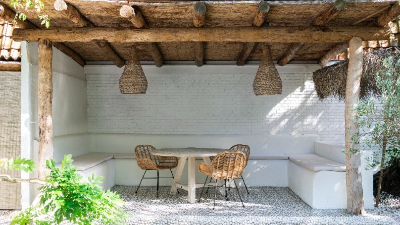 Sitzbereich im Garten mit Korbstühlen, Holzüberdachung und weiß gestrichenen Wänden