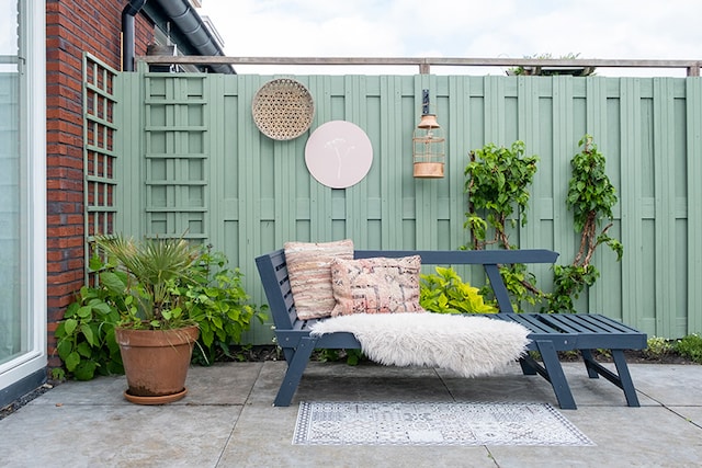 Groene schutting met blauwe tuinstoel en grijze tegels op de grond
