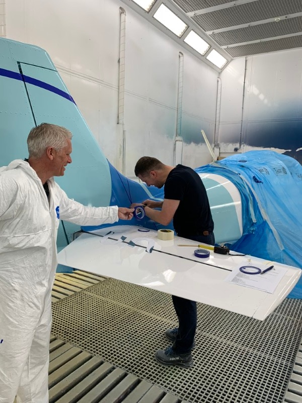 One technician assists another in taping off the tail of the aircraft for the next coat of paint.  