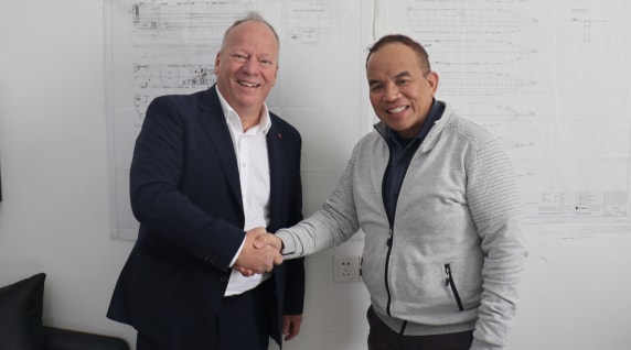 Two men wearing hard hats standing at a port with a Höegh Autoliners vessel in the background.