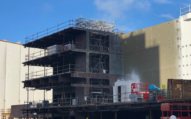Steel block section under scaffolding with workers preparing surfaces for coating application.