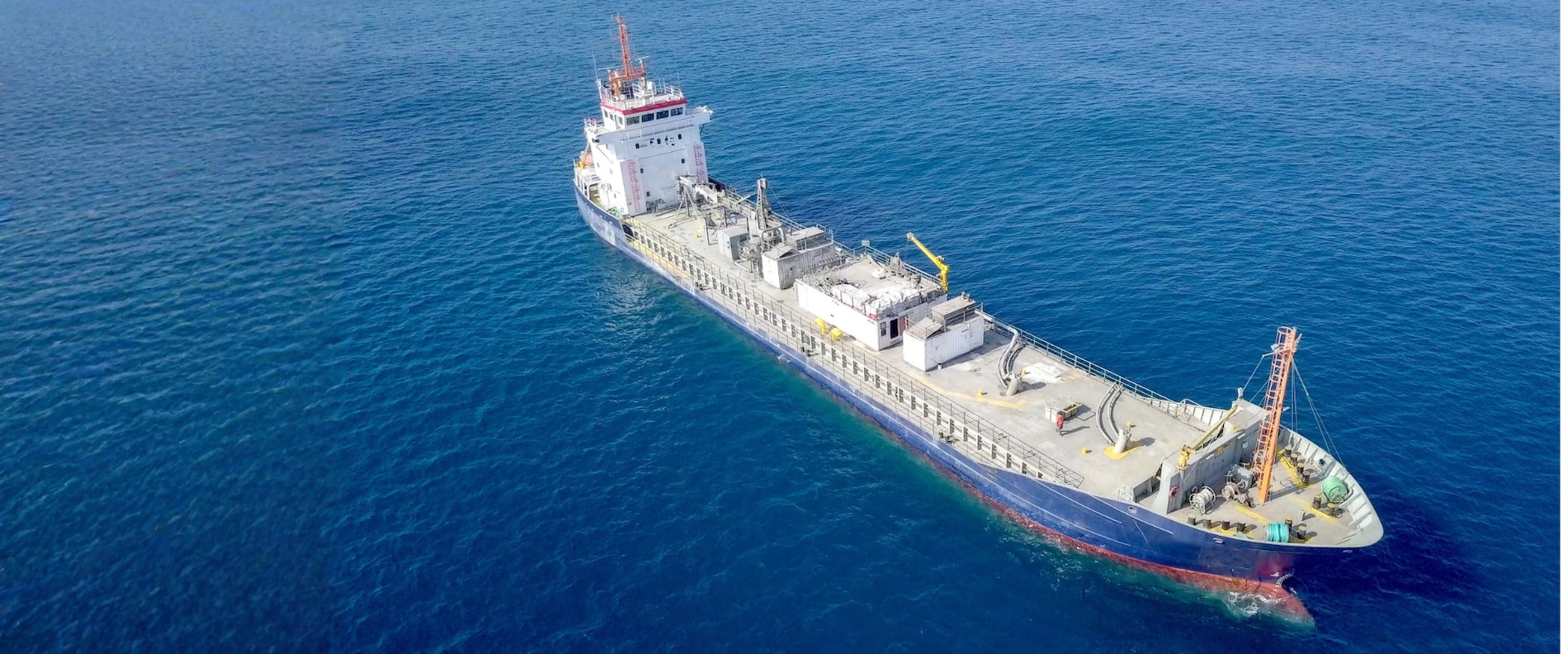 General cargo vessel sailing in open blue waters, aerial view.