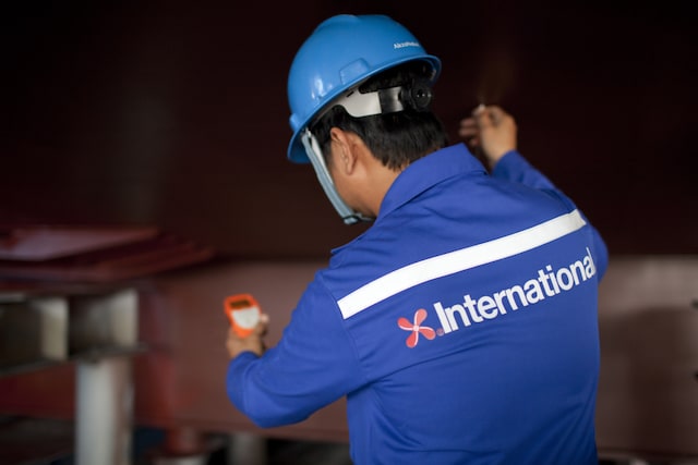 Worker wearing protective clothing and helmet using a handheld device on a vessel interior