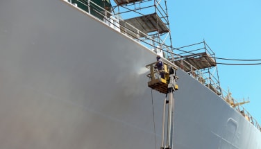 Ship hull under maintenance with coating being applied by technician