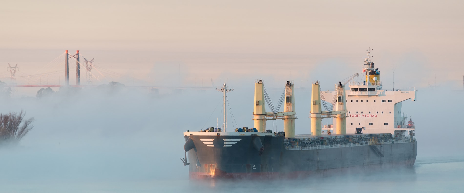 Bulk carrier ship navigating through fog near an industrial port