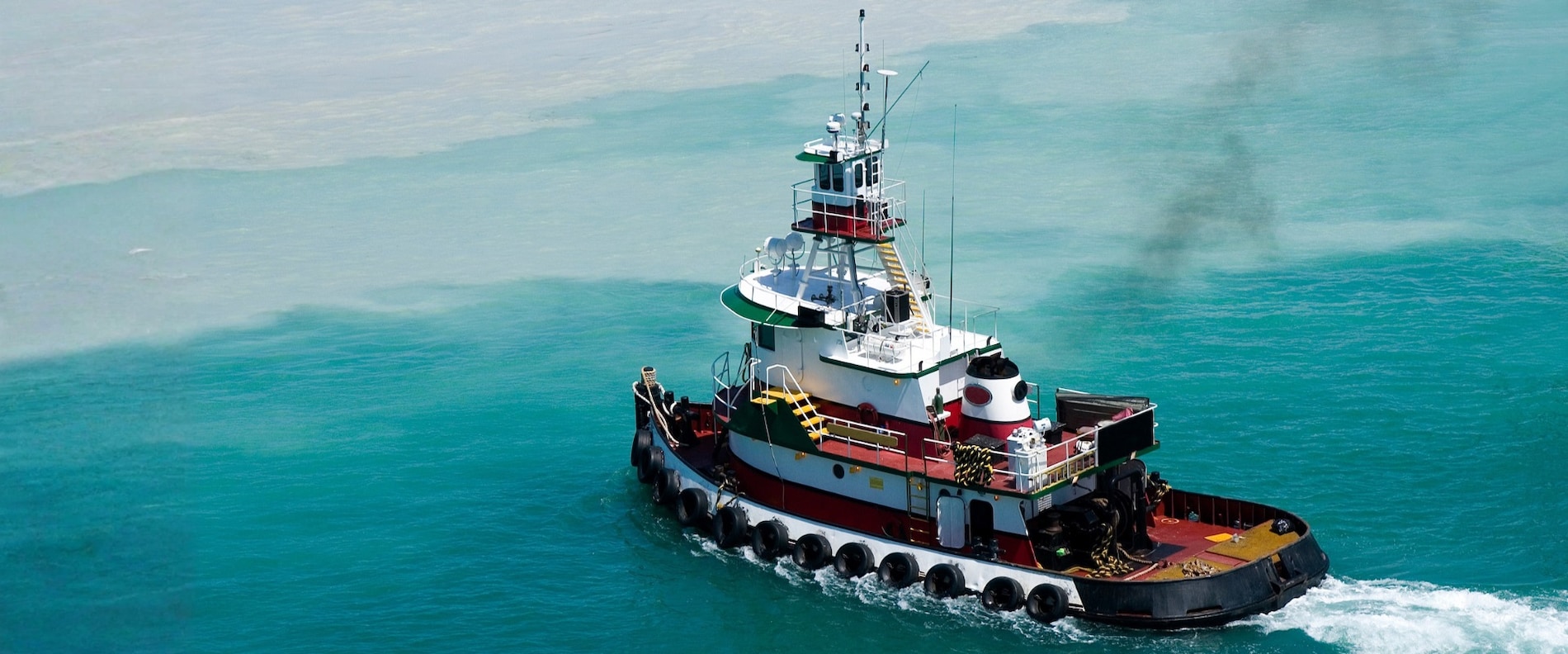 Tugboat operating in coastal waters, aerial view.