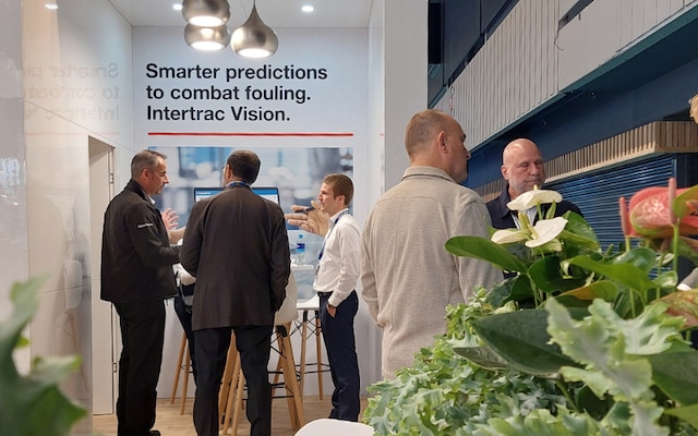 People talking inside the International Marine Coatings booth at Europort, with a wall display reading “Smarter predictions to combat fouling. Intertrac Vision.
