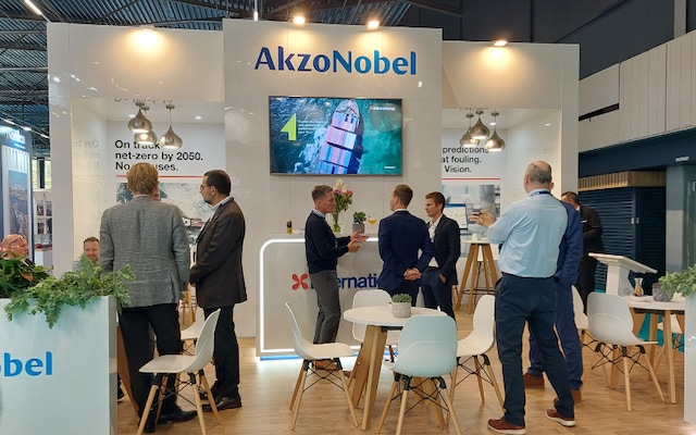 Several people stand and talk inside the International Marine Coatings booth at Europort. The booth features display screens and wall text about sustainability and Intertrac Vision.