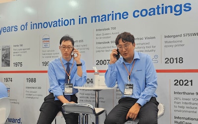 Team members seated in front of the “Over 140 Years of Innovation in Marine Coatings” timeline display.