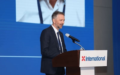 Darin Kirkwood speaking at the podium during Kormarine 2025, with the International Marine Coatings logo visible on stage.
