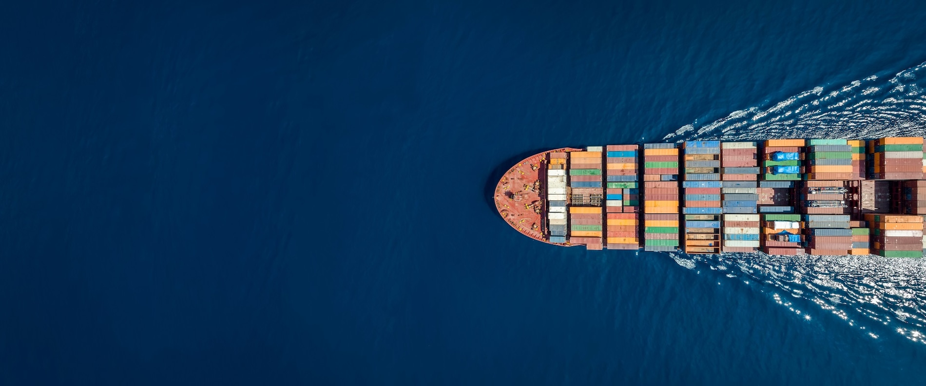Aerial view of a large cargo ship carrying colorful shipping containers across deep blue water.