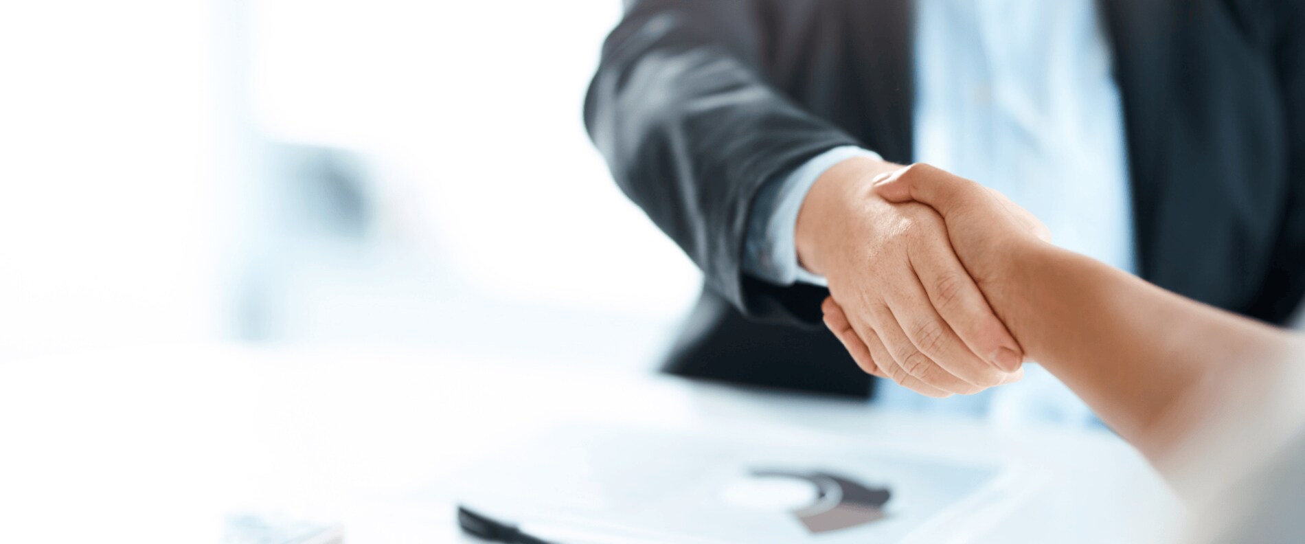 Close-up of two people shaking hands across a desk