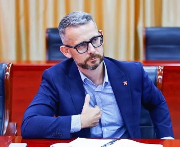 A man seated at a meeting  table with a notebook in front of him.  A nameplate reading ‘Rob Leslie’  is placed on the table.	