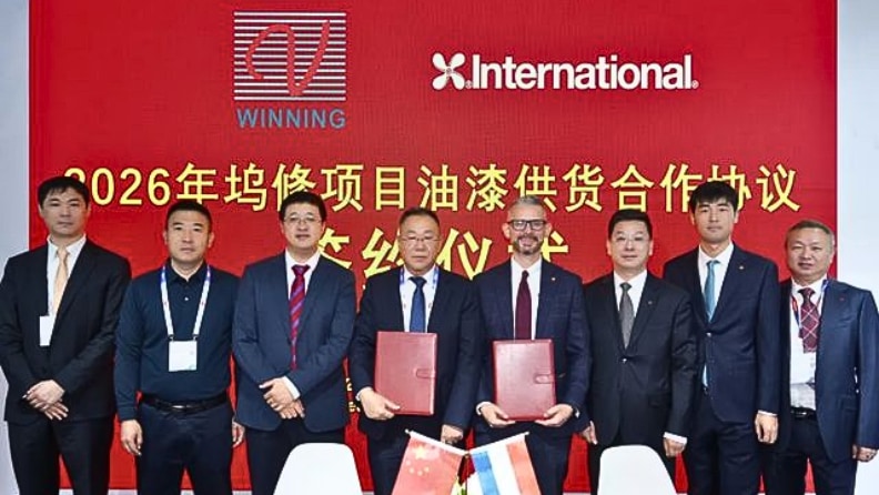 A group of representatives from International and Winning Shipping pose for a photo during a signing ceremony, with two people holding signed documents in front of a red backdrop showing both company logos.