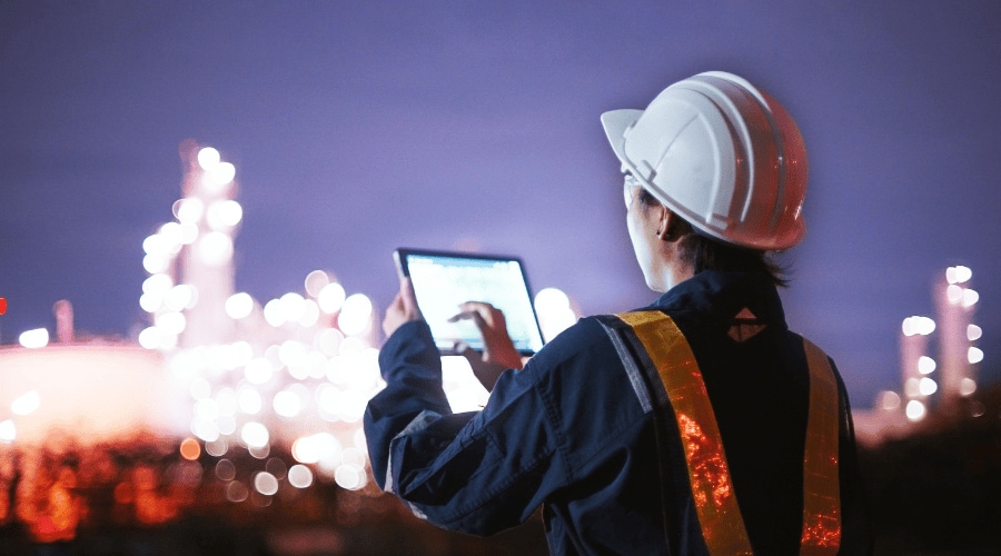 Person holding a digital device at an industrial facility with steel framework in the background.