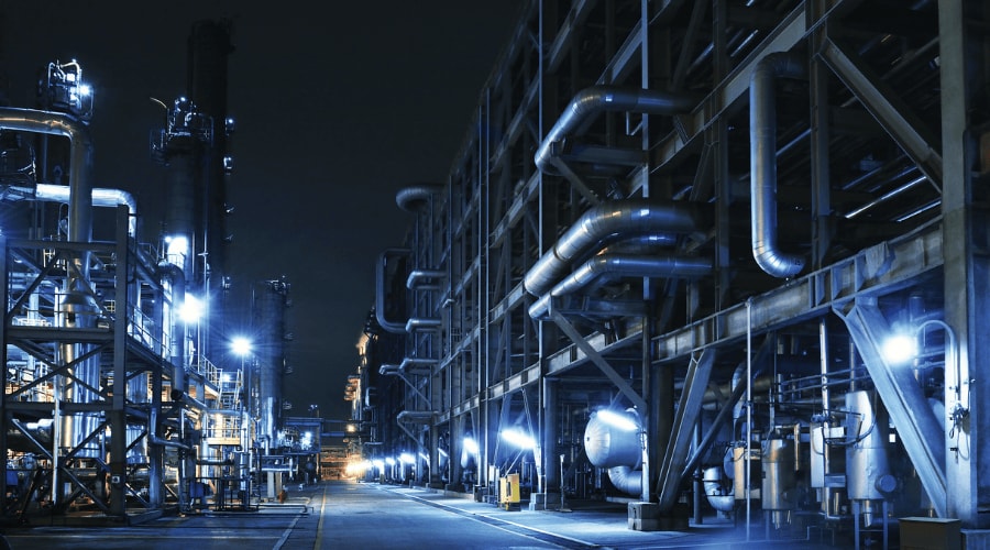 Industrial facility at night with illuminated steel structures, pipes, and processing equipment.