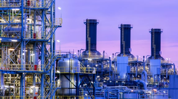 Industrial refinery complex with pipes, tanks, and chimneys under a purple evening sky.