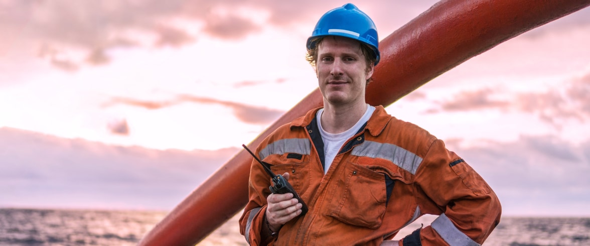 Engineer wearing a hard hat working on a laptop outdoors at sunset with wind turbines in the background.