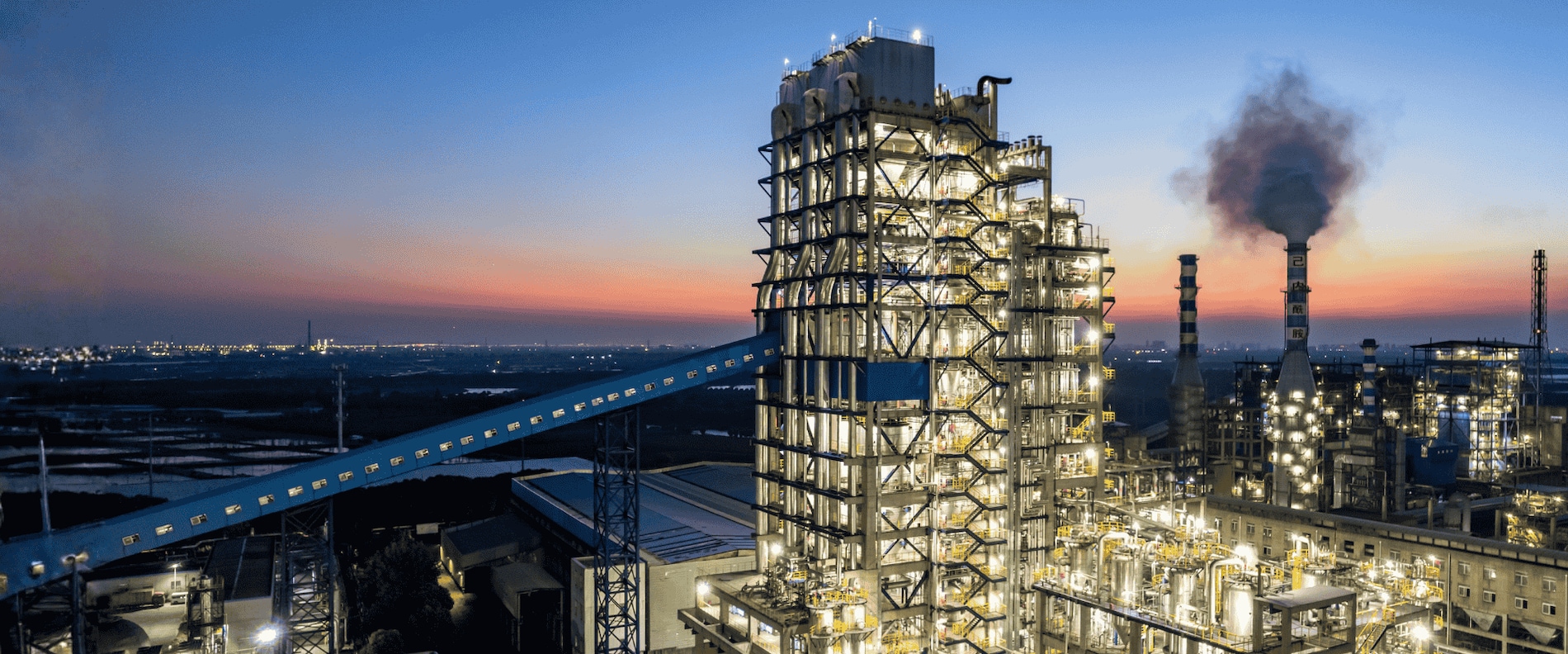 Large onshore industrial plant at sunset showing steel structures and refinery equipment.