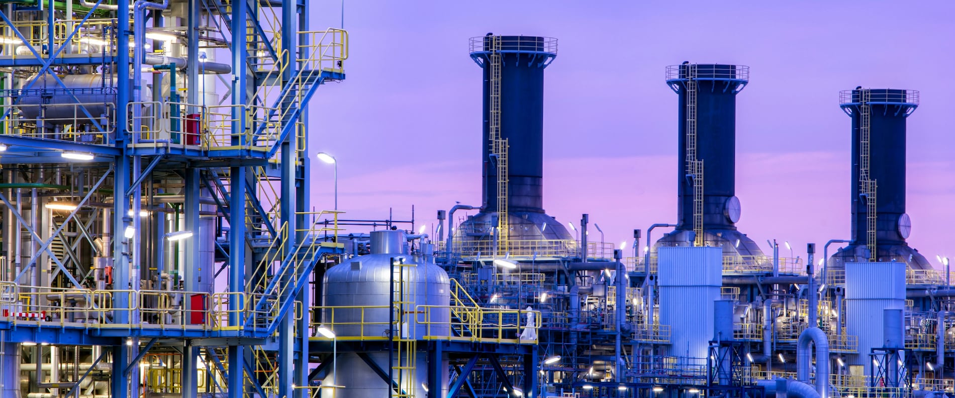 Industrial oil and gas processing facility with pipes and towers at dusk