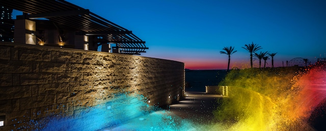 Curved stone wall with warm lighting at sunset, leading to a palm-lined beach