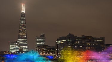 Night view of The Shard in London with city lights reflecting on the river.