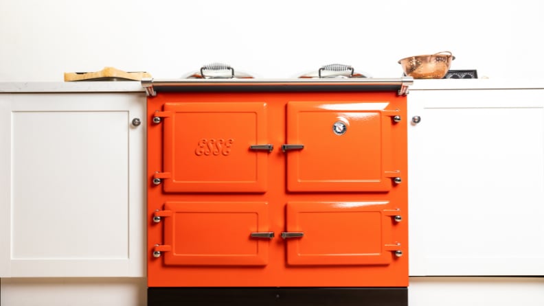 Bright orange range cooker between white kitchen cabinets