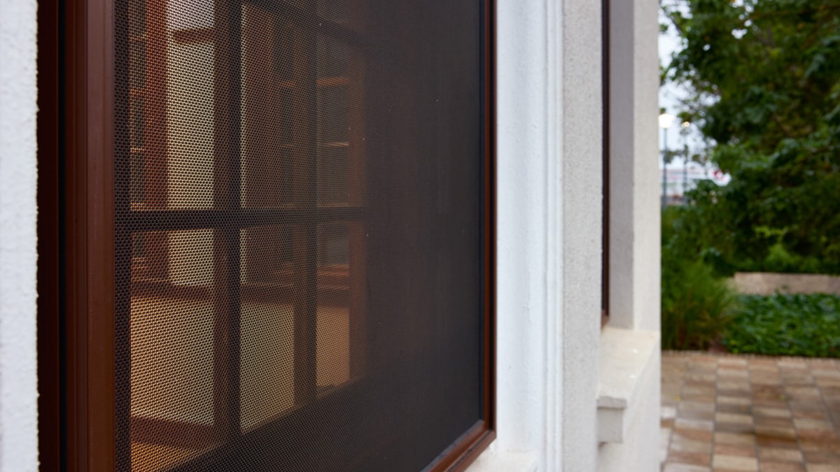 Close-up of a brown security mesh screen on a window with garden view outside.