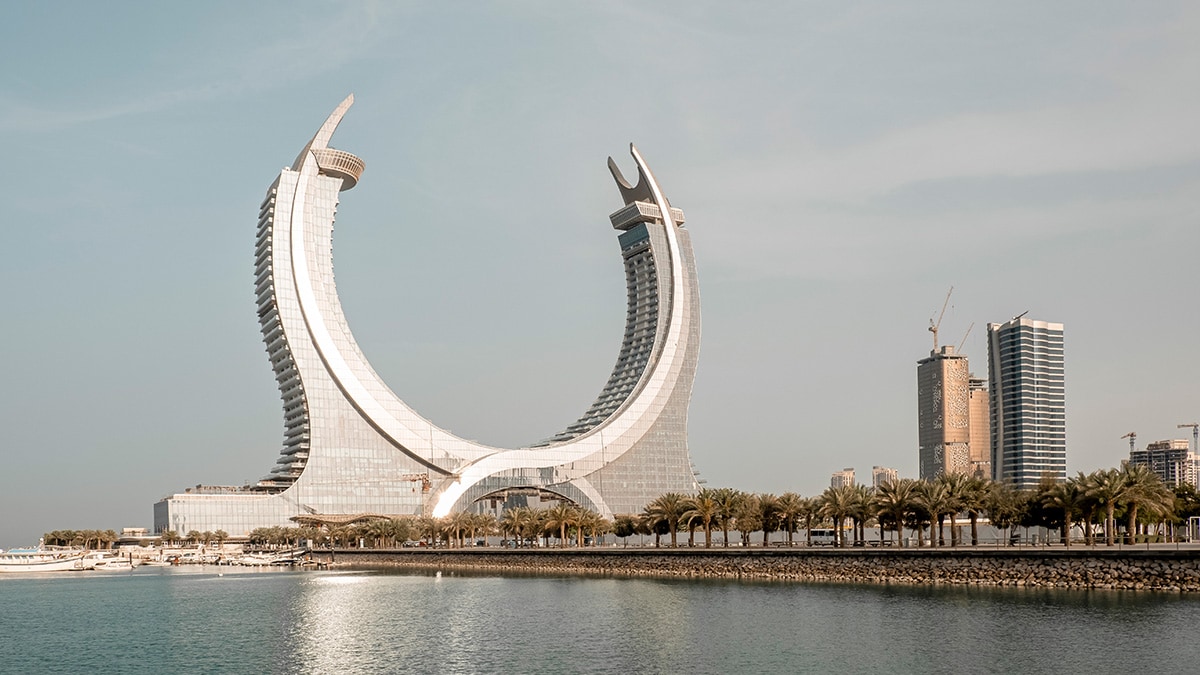 A unique arch-shaped architectural structure surrounded by water and city buildings in Qatar.