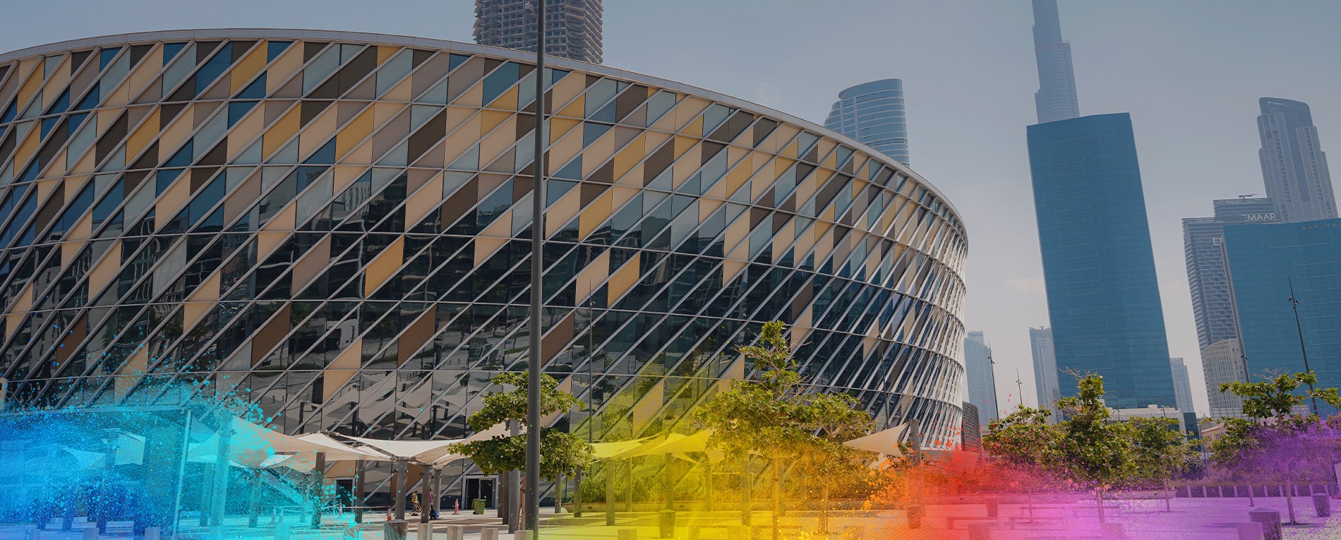 A modern, circular arena with a striking diamond-patterned facade, set against a city skyline featuring tall skyscrapers.
