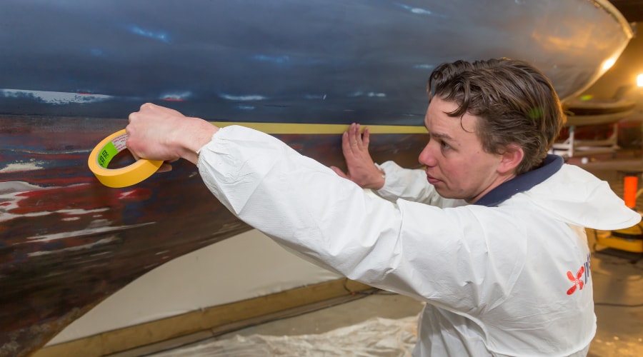 Person applying masking tape to the hull of a boat during maintenance preparation.