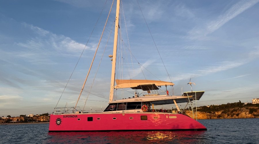 The restored catamaran afloat on the water with a pink hull following completion of the refit.