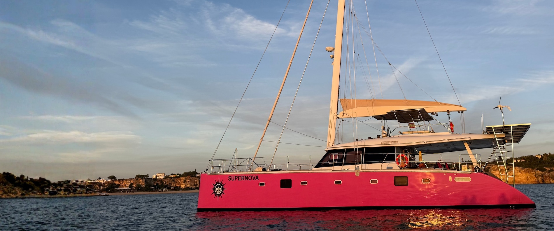 The restored catamaran afloat on the water with a pink hull following completion of the refit.
