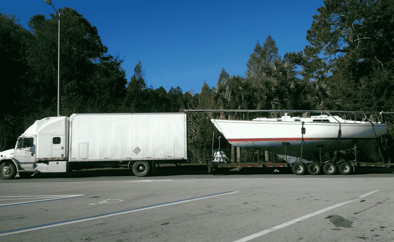 A sailboat loaded onto a trailer being transported by a large truck