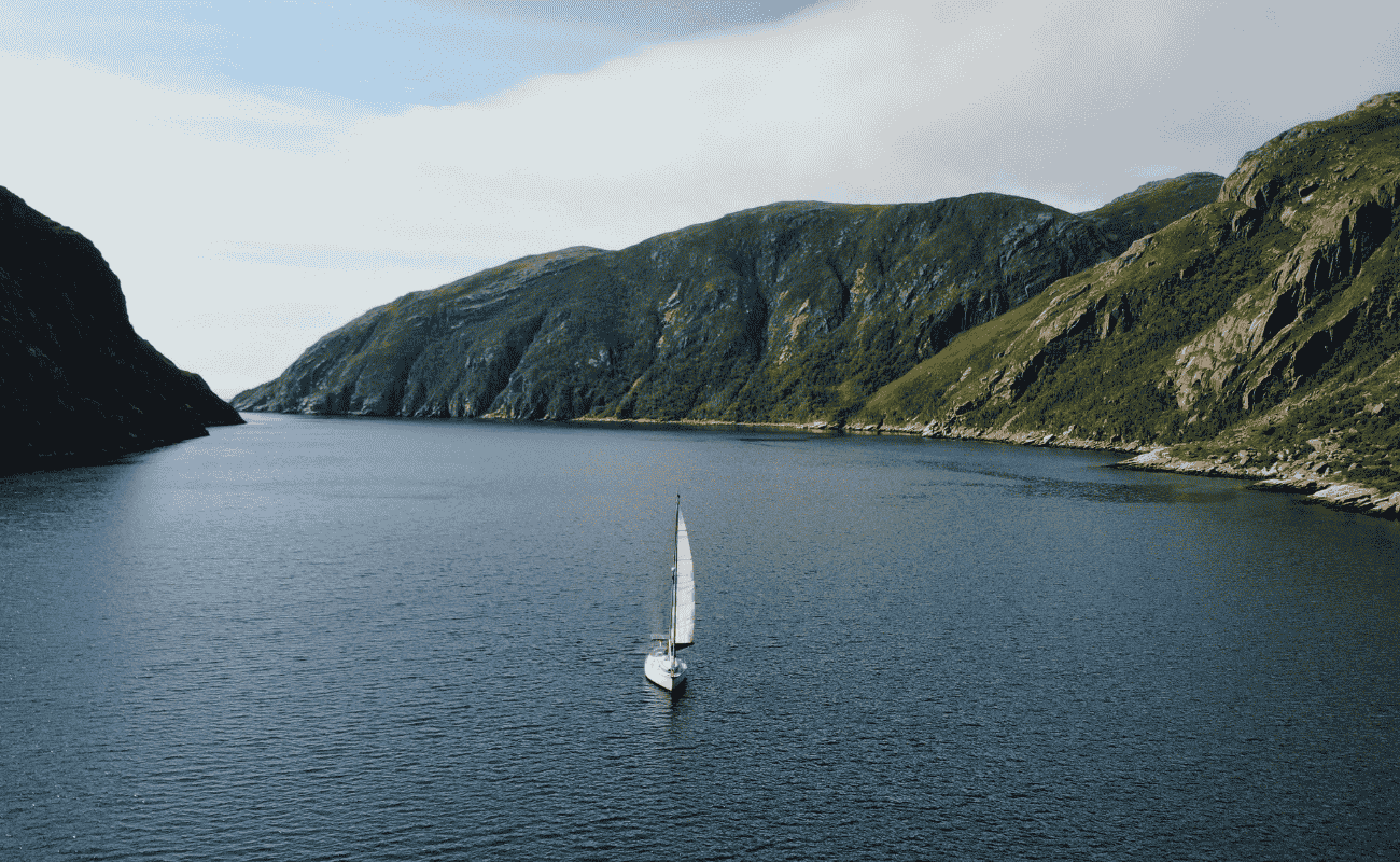 Sailing UMA’s yacht under sail in a wide fjord surrounded by steep green mountains
