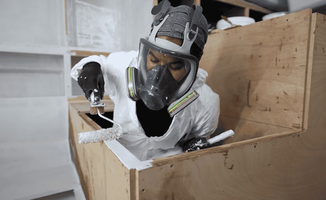Person in protective gear applying primer inside a wooden boat interior