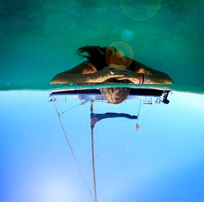 En person flyter vid vattenytan bredvid en segelbåt, med båtens skrov synligt under det klara blå vattnet.