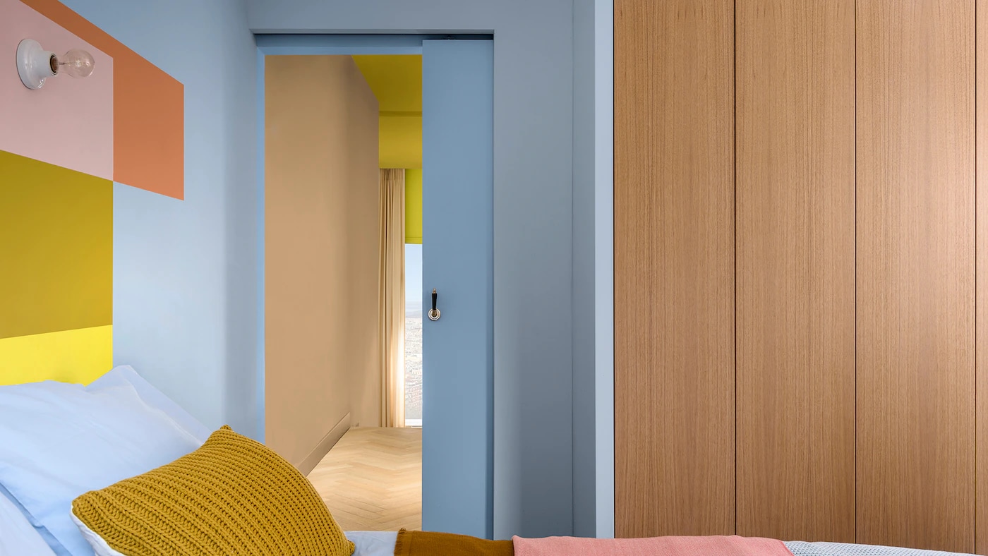 Quarto compacto decorado com a cor Melodia Suave da Tintas Coral. Uma parede de cabeceira com tons rosados e amarelos podem trazer destaque ao espaço 