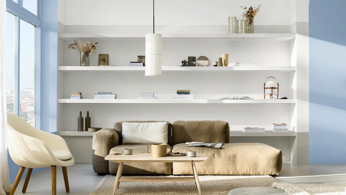 Sala de estar decorada com a cor Melodia Suave da Tintas Coral em detalhes composto com neutros. Os móveis neutros em composição com o azul transformam o ambiente, oferecendo leveza e claridade. 